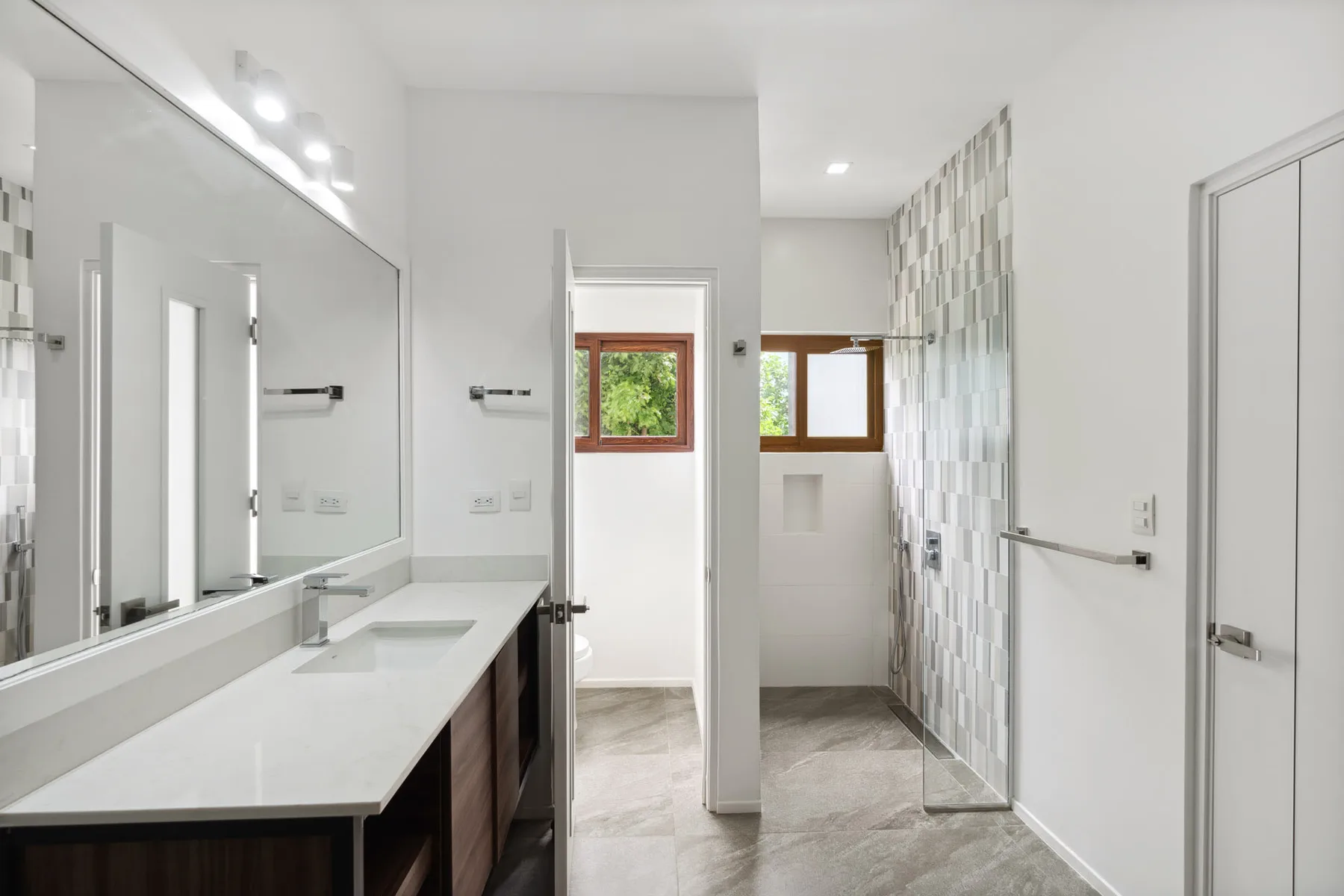 A bright bathroom with a long vanity, large mirror, and tiled walls.