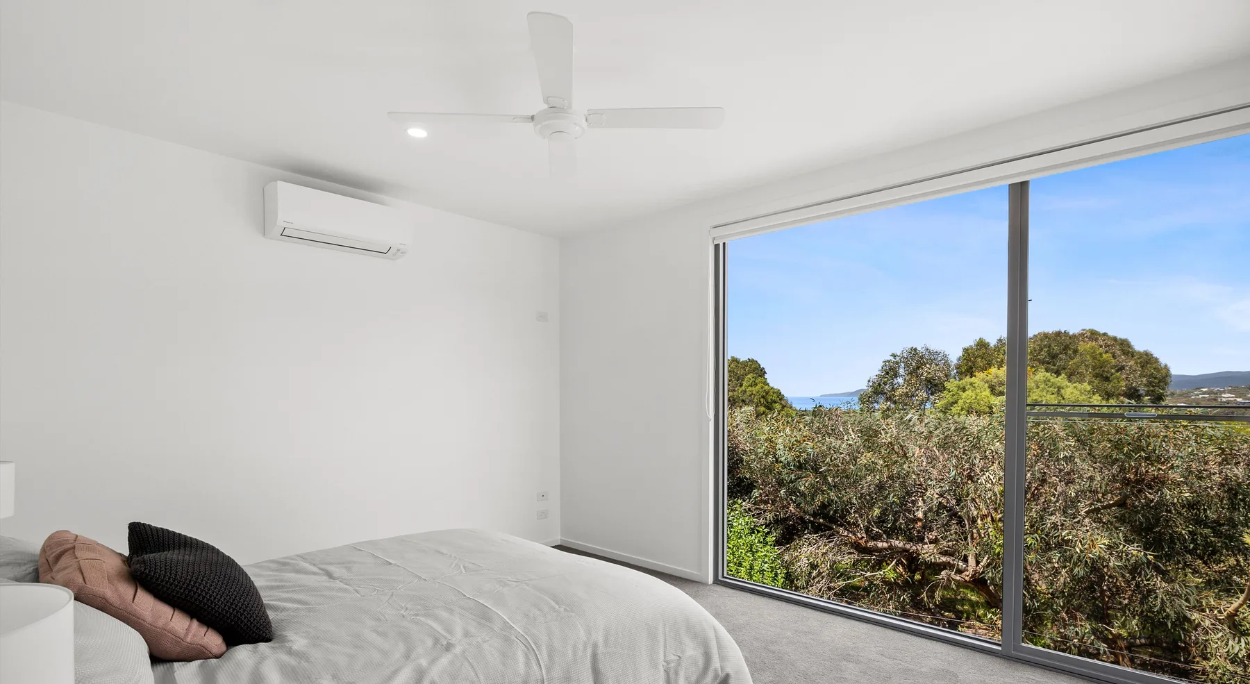 Un dormitorio luminoso con una cama junto a una gran ventana con vistas a la vegetación.