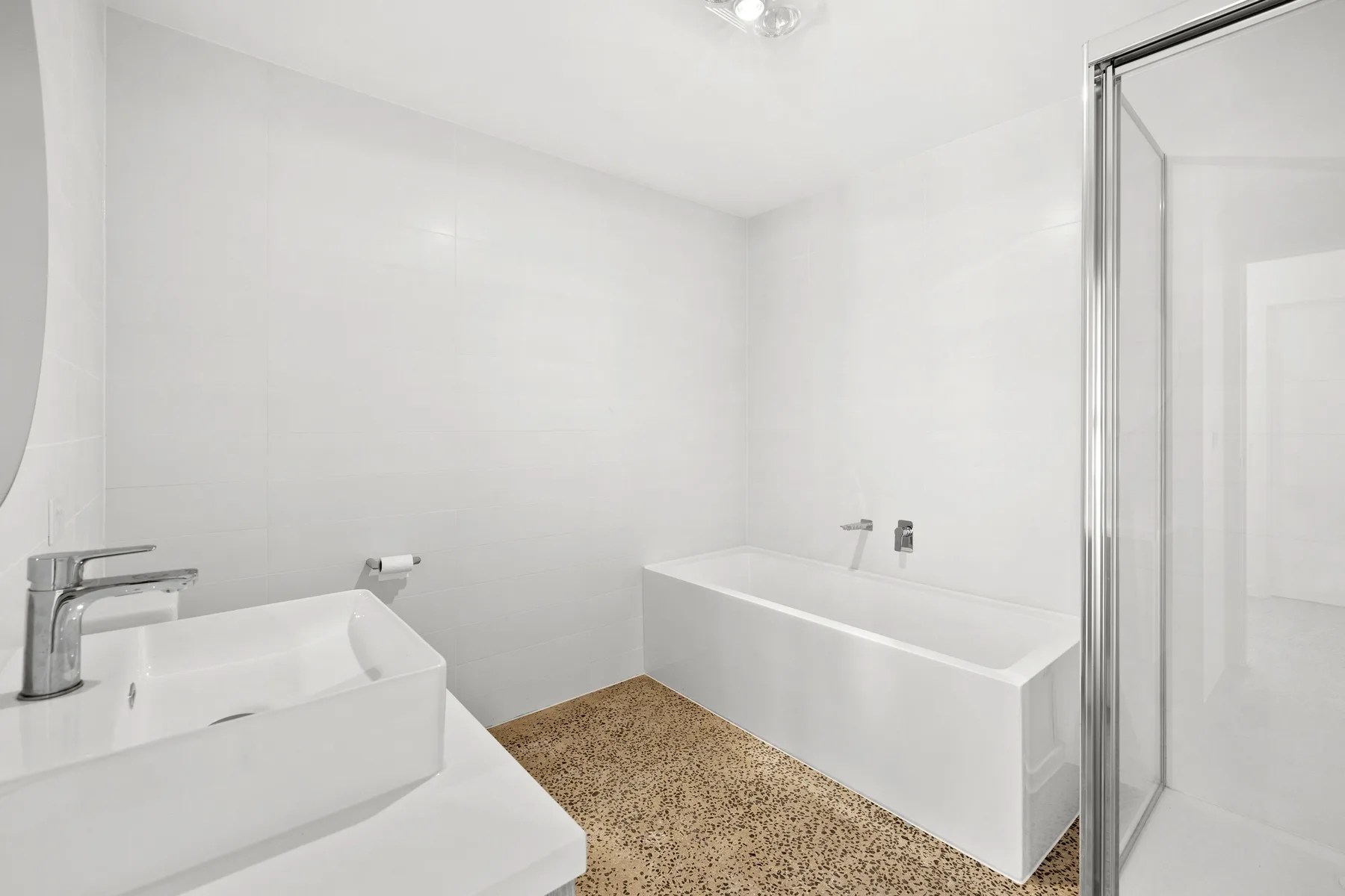 Un baño luminoso con bañera, lavabo y una mampara de ducha de vidrio.