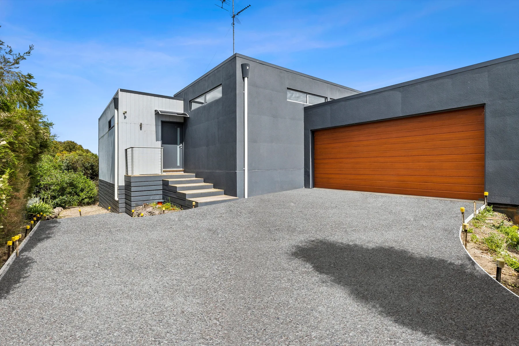Exterior de una casa moderna con una amplia entrada pavimentada y una puerta de garaje de madera.