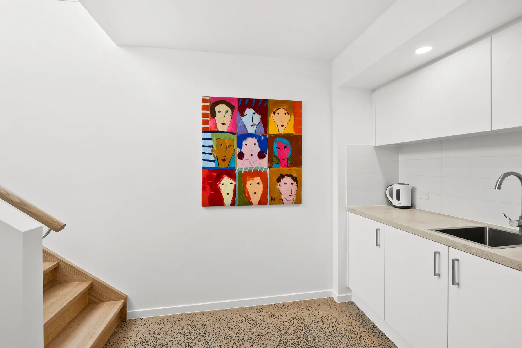 Una cocina luminosa con gabinetes blancos, una encimera y arte colorido en la pared.