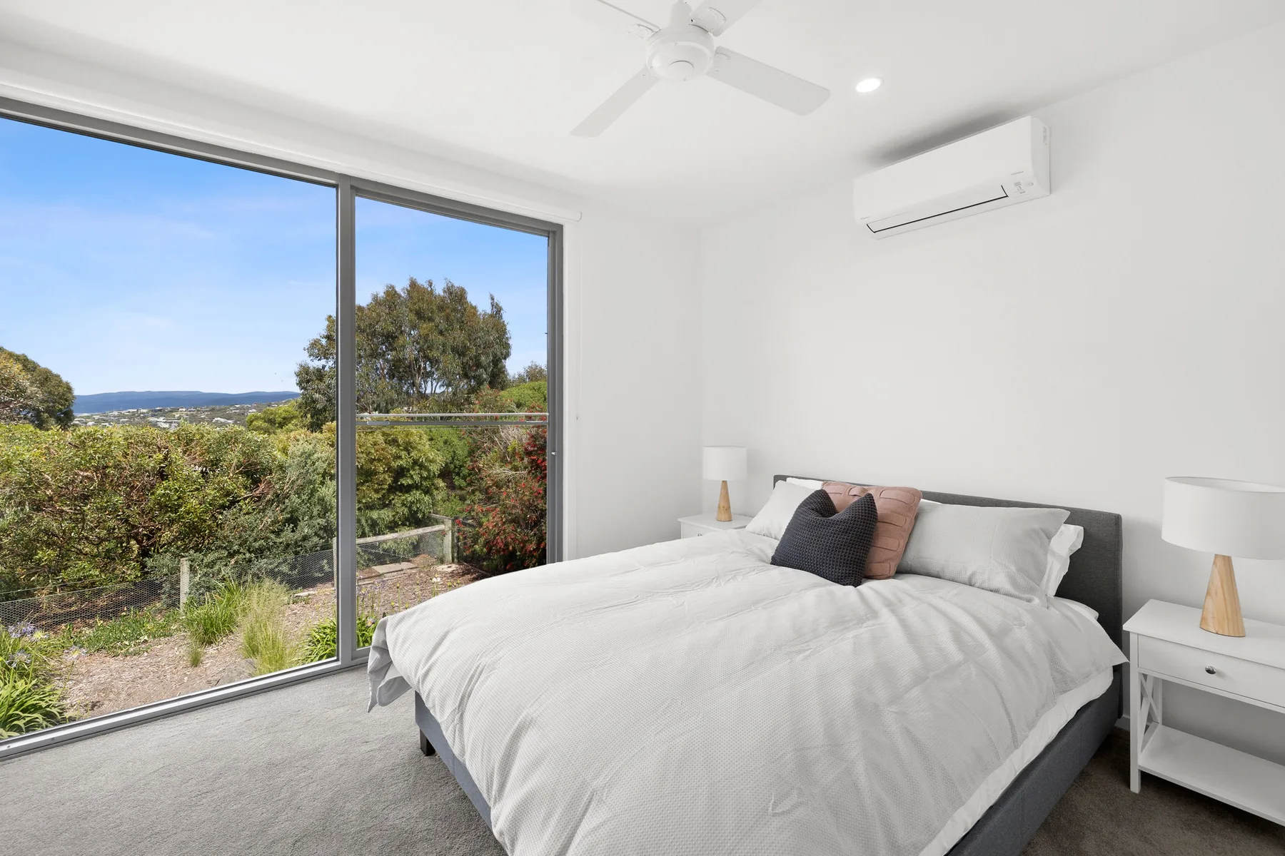 Un dormitorio luminoso con una cama grande junto a una amplia ventana con vistas a la vegetación.