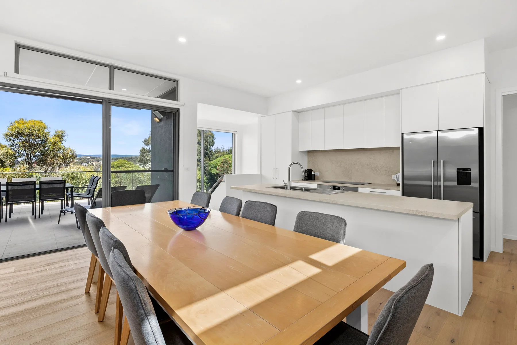 Una cocina y comedor luminosos con una mesa de madera y grandes ventanas.