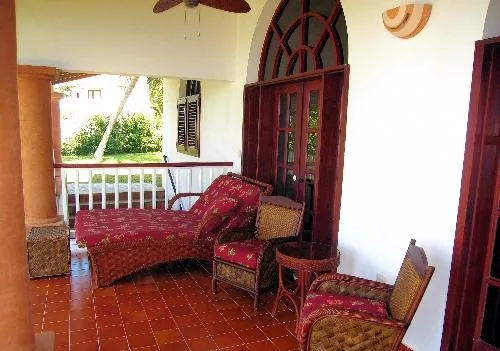 A covered porch with red patterned seating and a tall arched wooden doorway.