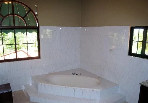 A bathroom with a built-in corner bathtub and tiled walls.