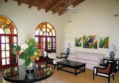 A bright living room has a white sofa, dark tables, and colorful artwork.