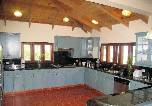 A kitchen with blue cabinets, dark countertops, and a wood-beamed ceiling.