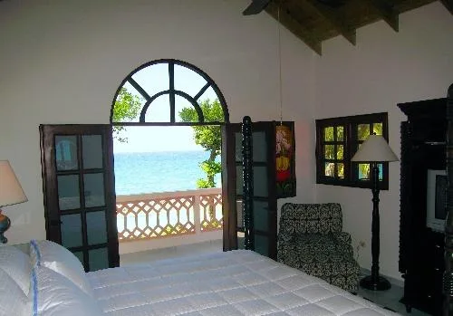 A bedroom opens onto a balcony overlooking the sea, with a bed in the foreground.