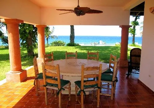 A covered patio with a dining table overlooks a grassy lawn and the ocean.