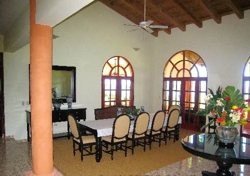 A dining area with a long table and chairs beneath exposed wooden ceiling beams.