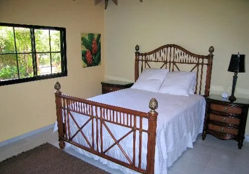 A bedroom with a wooden bed dressed in white linens and a window overlooking greenery.