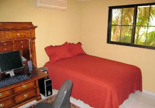 A bedroom with a red-covered bed and a window overlooking greenery.