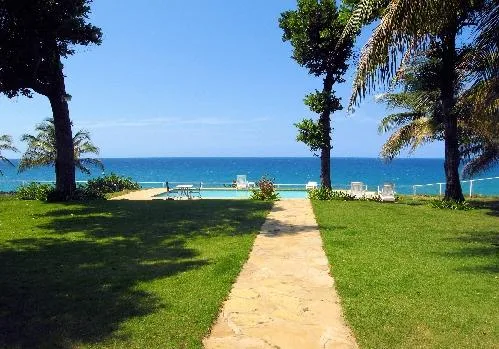 A garden path leads toward a swimming pool and the ocean.