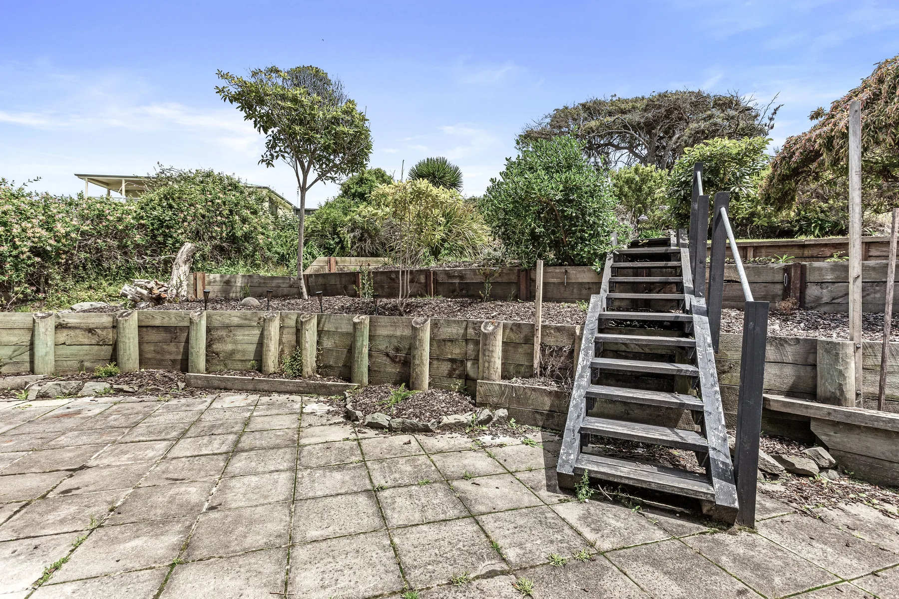 Un patio exterior pavimentado con una escalera de madera que sube a una zona ajardinada elevada.