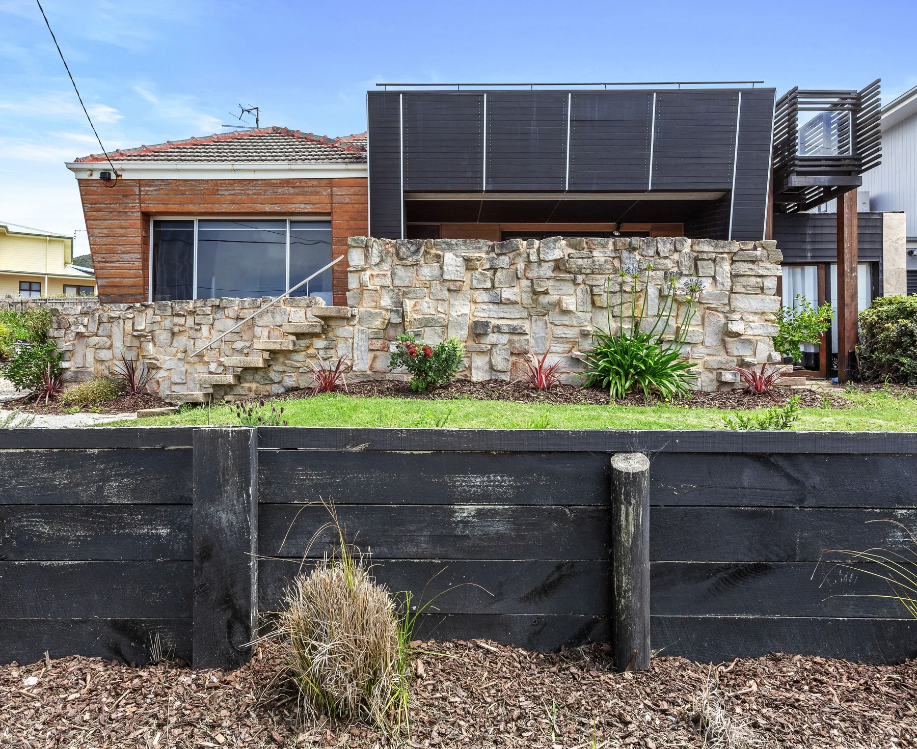 Una casa moderna se alza detrás de un muro bajo de piedra y un jardín ajardinado.