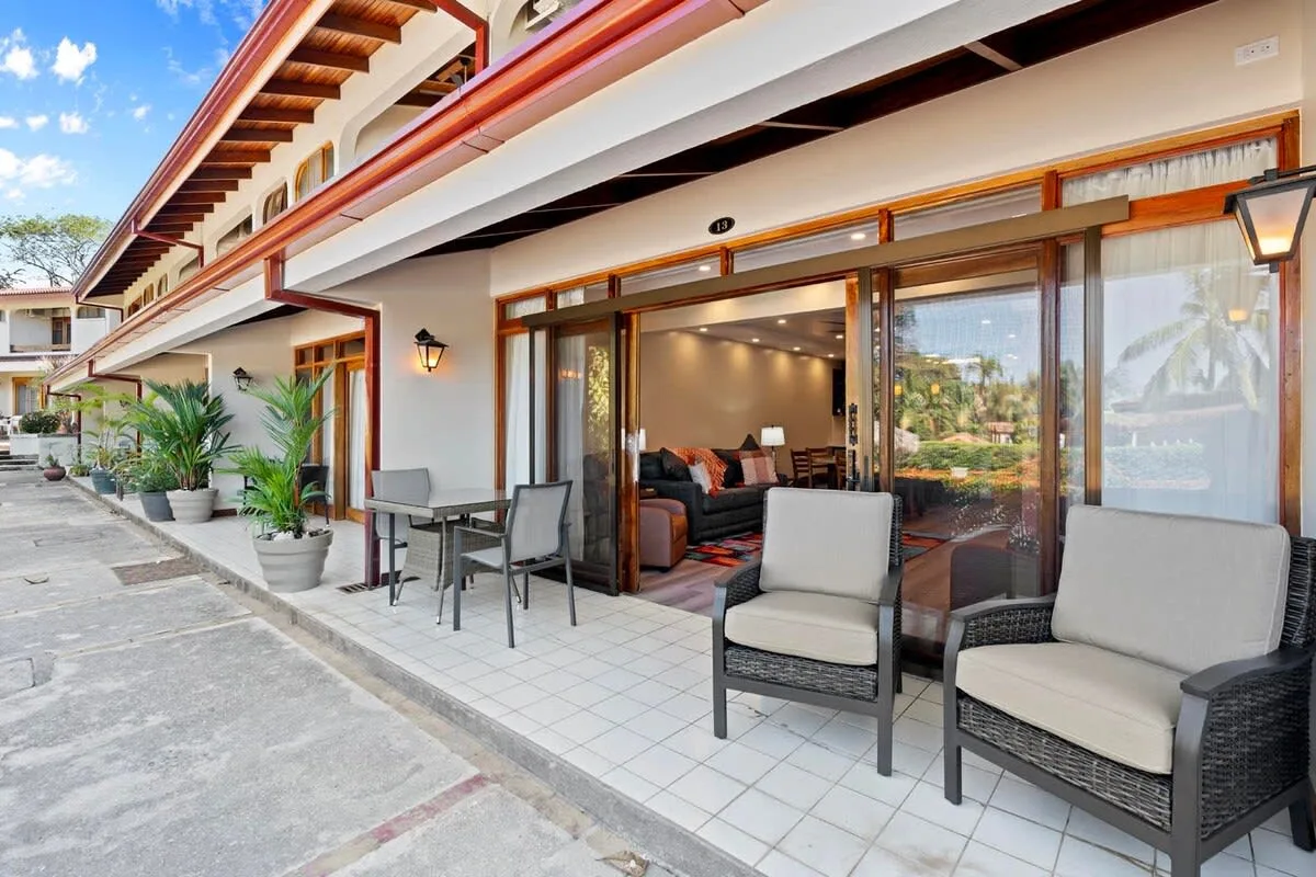 A tiled patio with outdoor seating sits outside a room with wide glass doors.