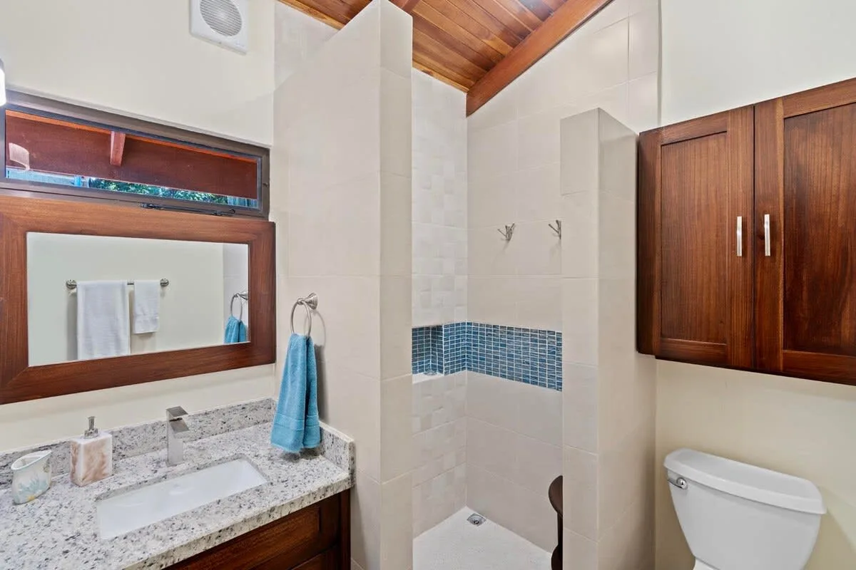 A tiled bathroom with a sink, mirror, shower area, and toilet.
