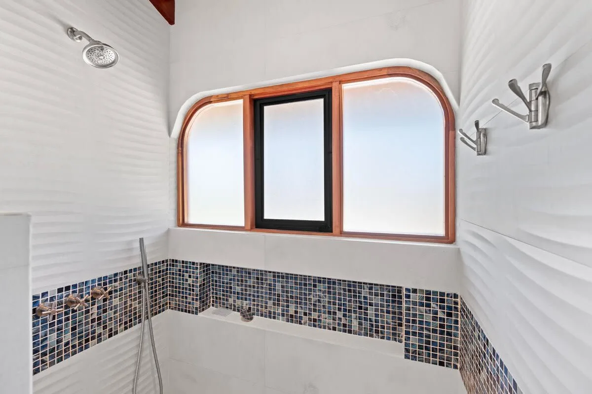 A tiled bathroom with a showerhead and an arched window.