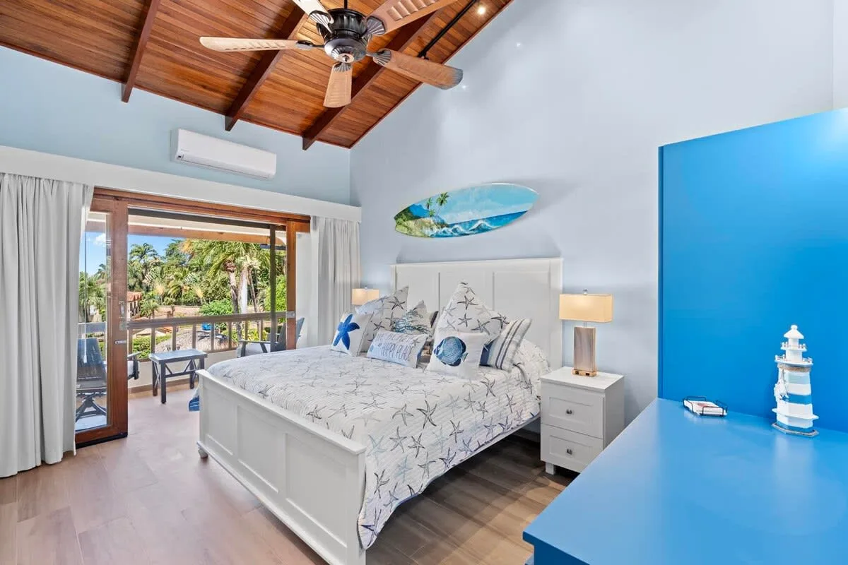 A bedroom with a white bed, blue furnishings, and a wood-paneled ceiling.