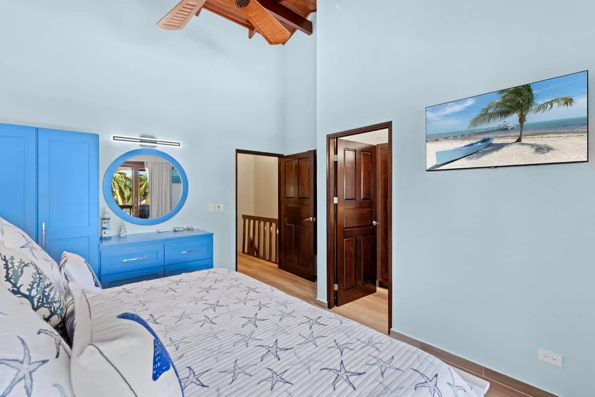 A bedroom with a blue bedspread, blue dresser, and framed beach picture.