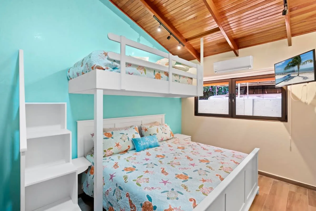 A bedroom with bunk beds, colorful bedding, and a wooden ceiling.