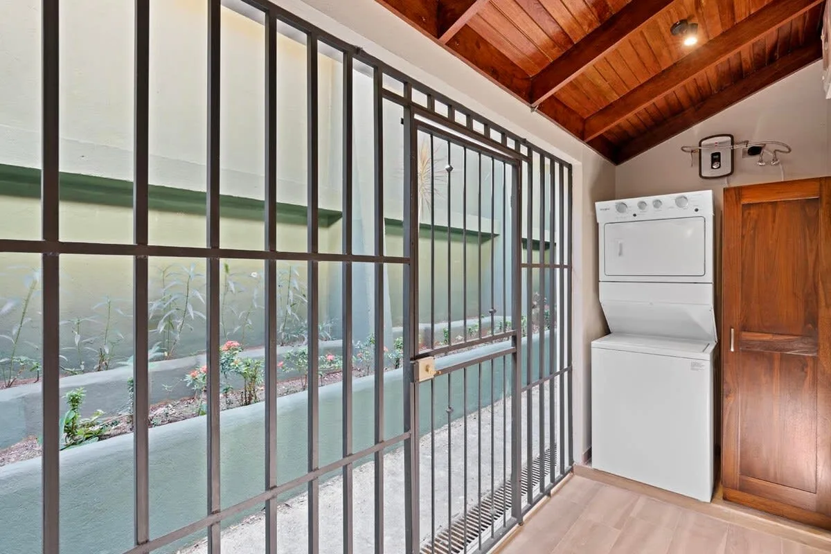 A laundry area with a stacked washer and dryer beside a barred glass door.
