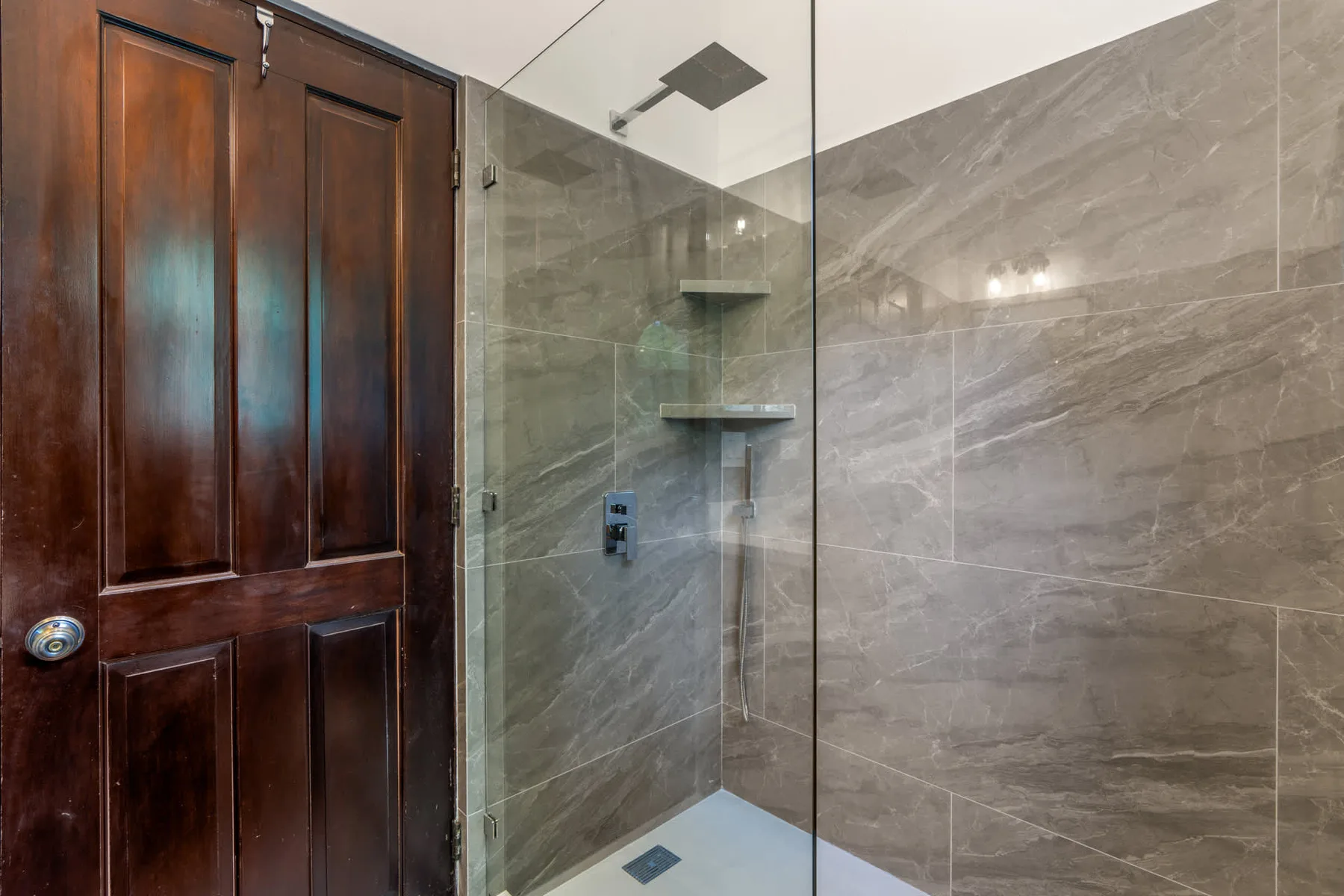 A tiled bathroom shower with a glass panel and built-in wall shelves.