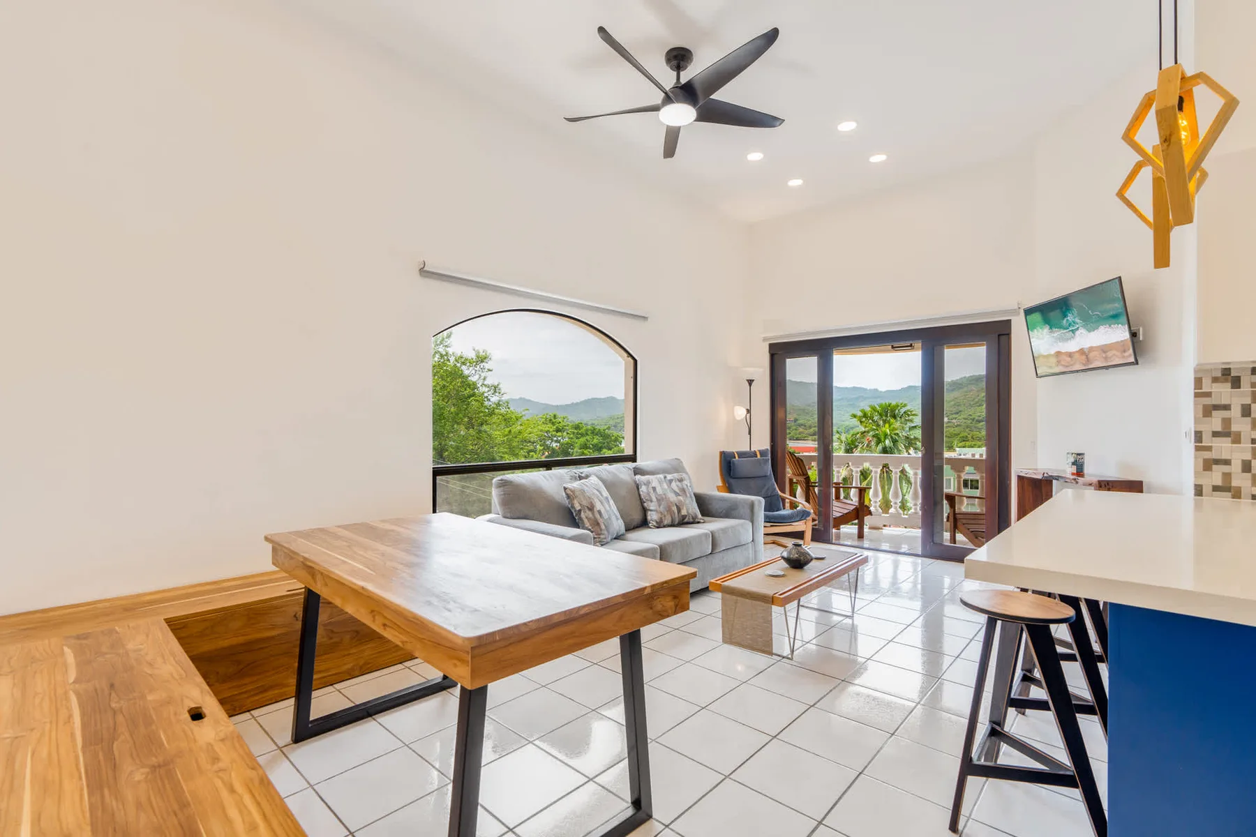 Open-plan living area with seating, a dining table, and glass doors opening onto a balcony.