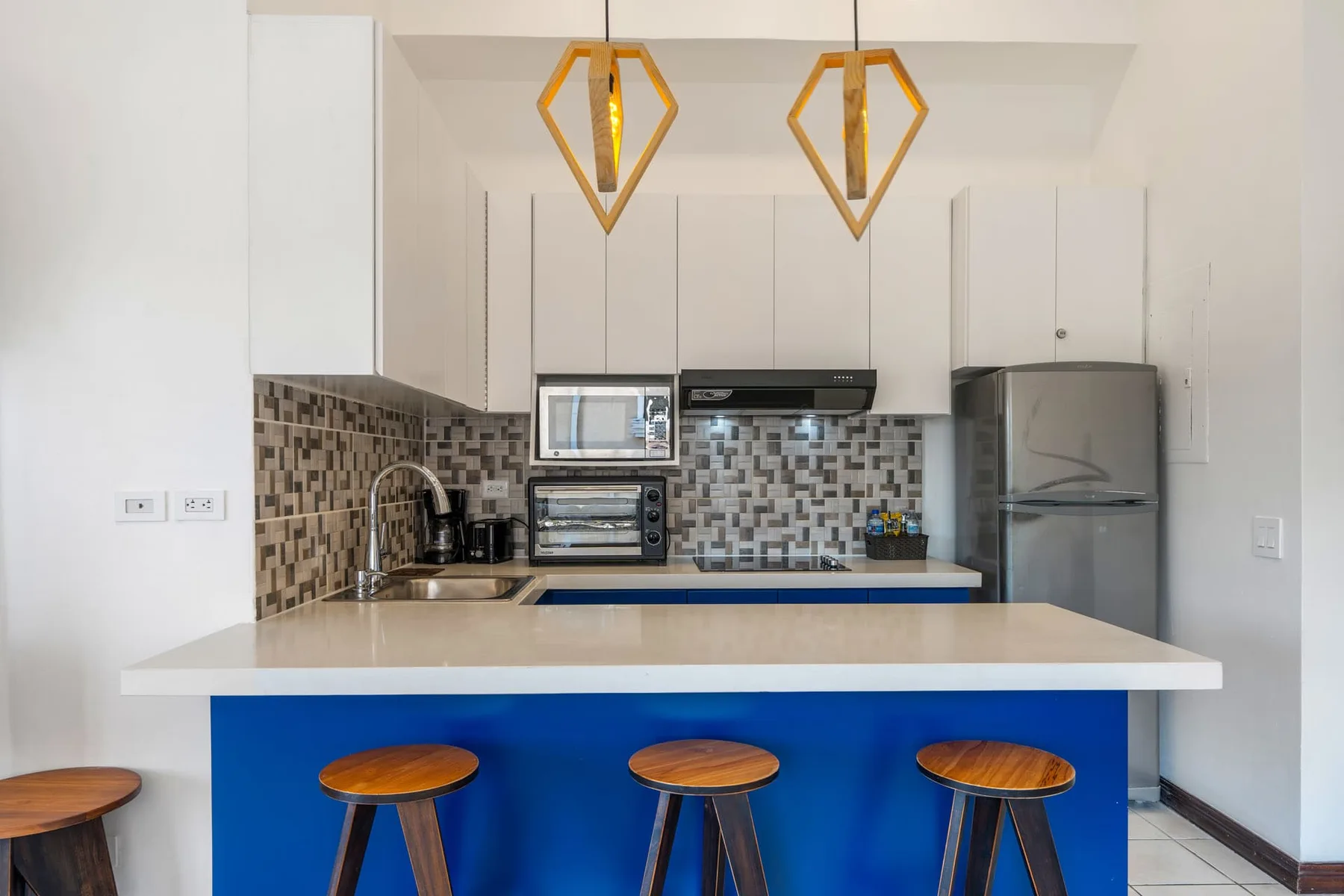 A bright kitchen with a blue breakfast bar and three wooden stools.