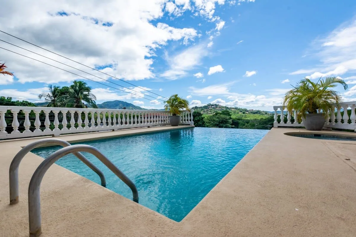 Shared amenity: An outdoor swimming pool with a paved deck and palm trees.