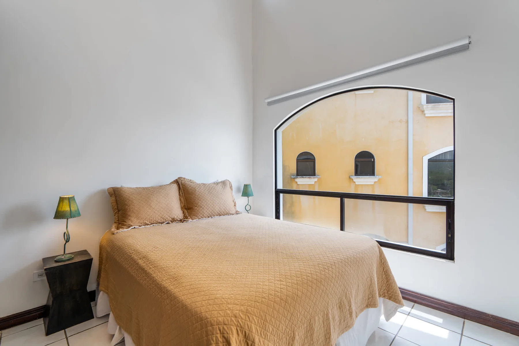 A bedroom with a bed beside a large arched window.