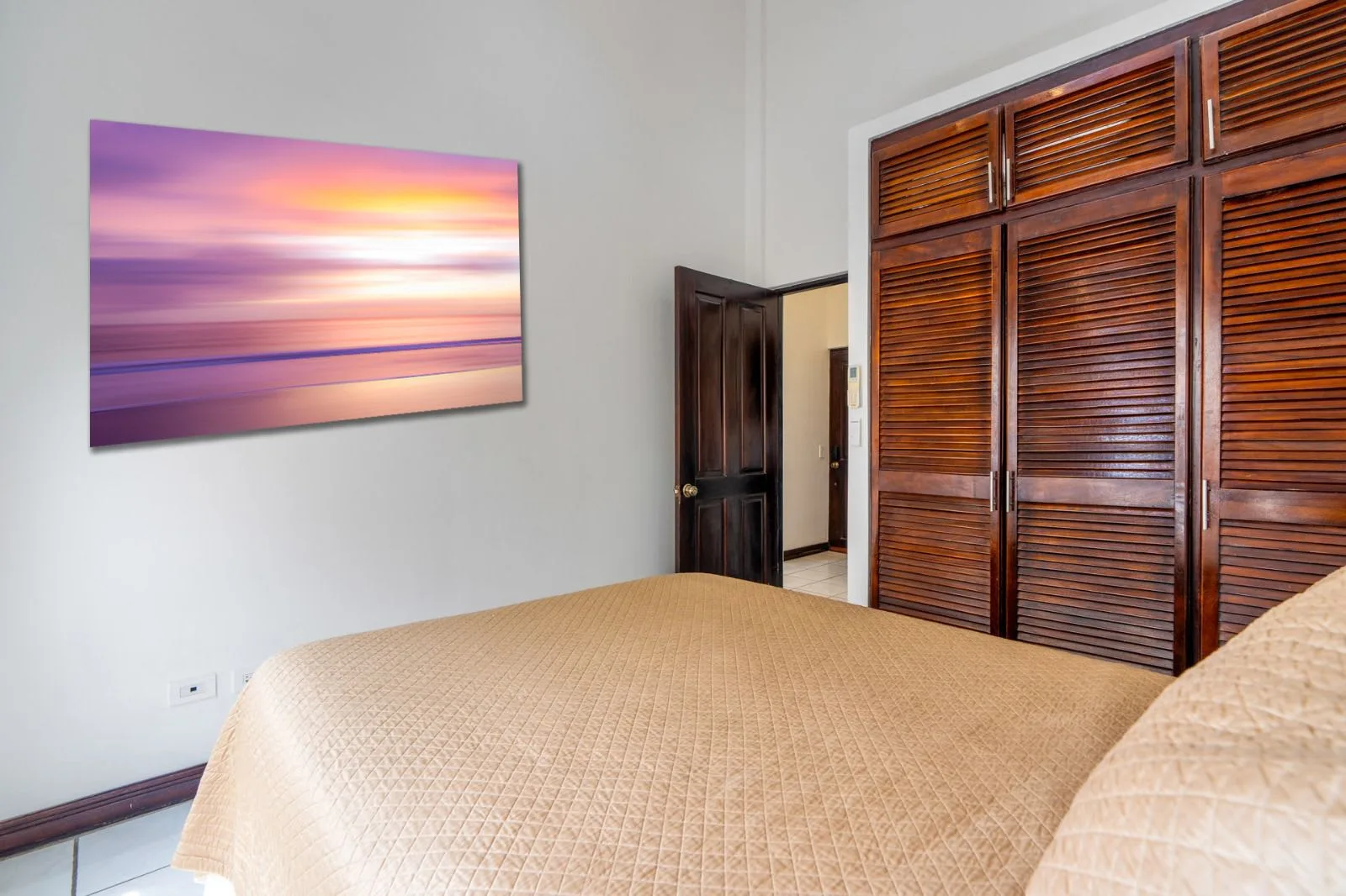 A bedroom with a neatly made bed and wooden louvered closet doors.
