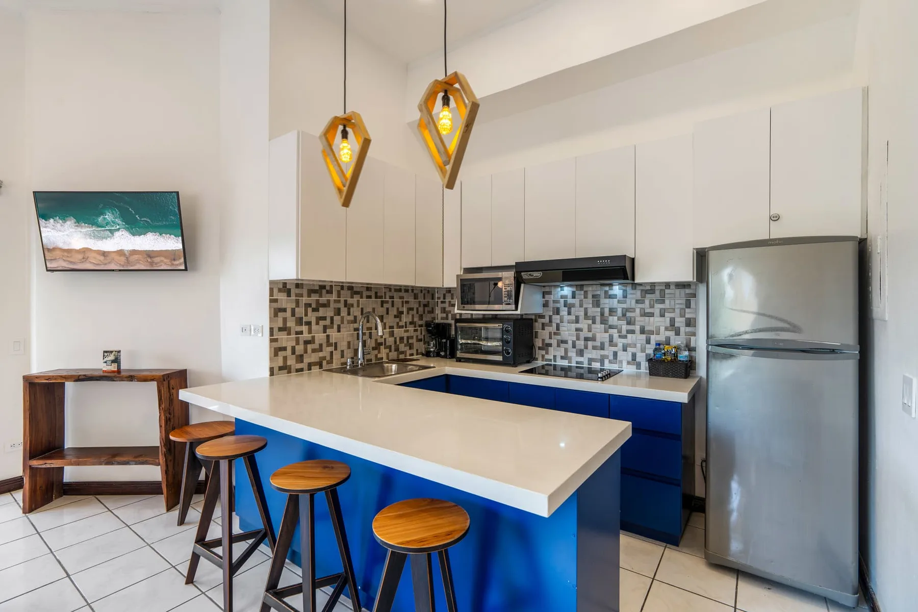 A bright kitchen with a blue island, bar stools, and stainless steel appliances.