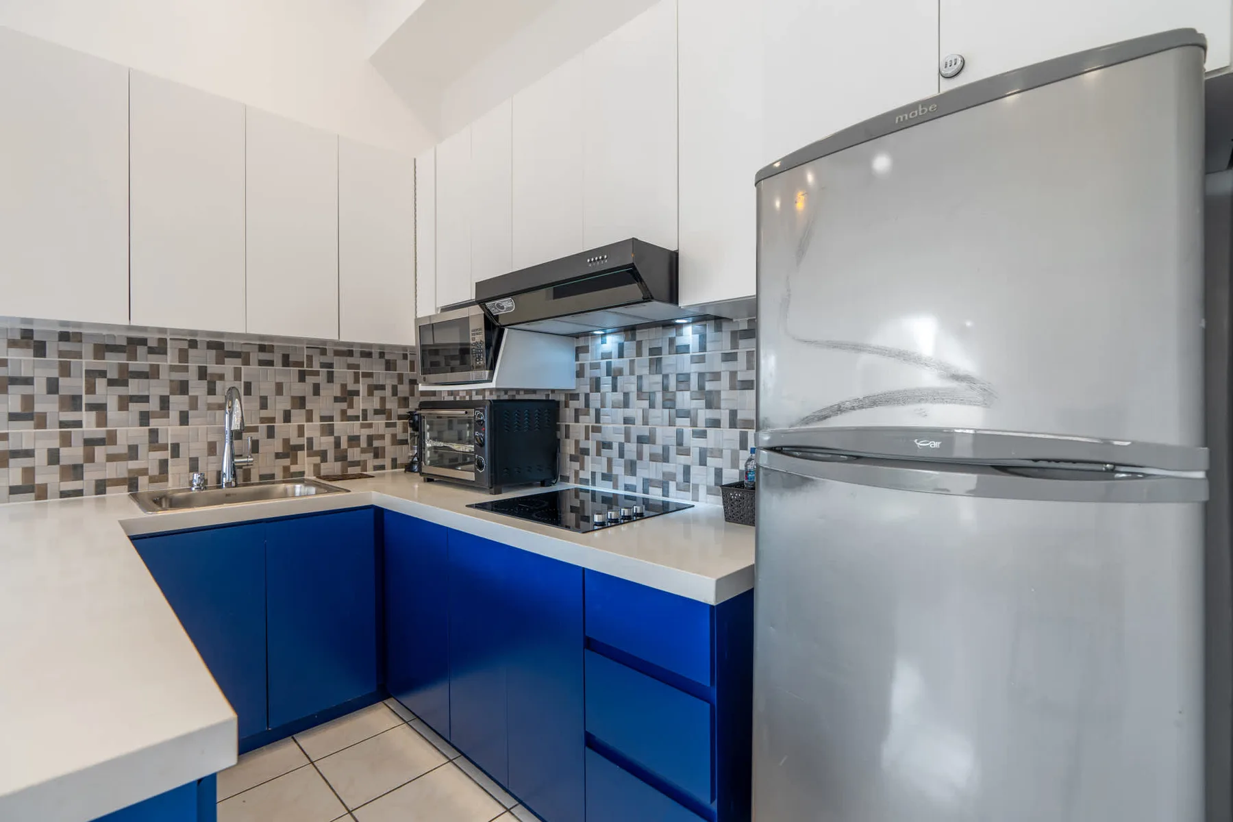 A kitchen with blue lower cabinets, a tiled backsplash, and stainless steel appliances.