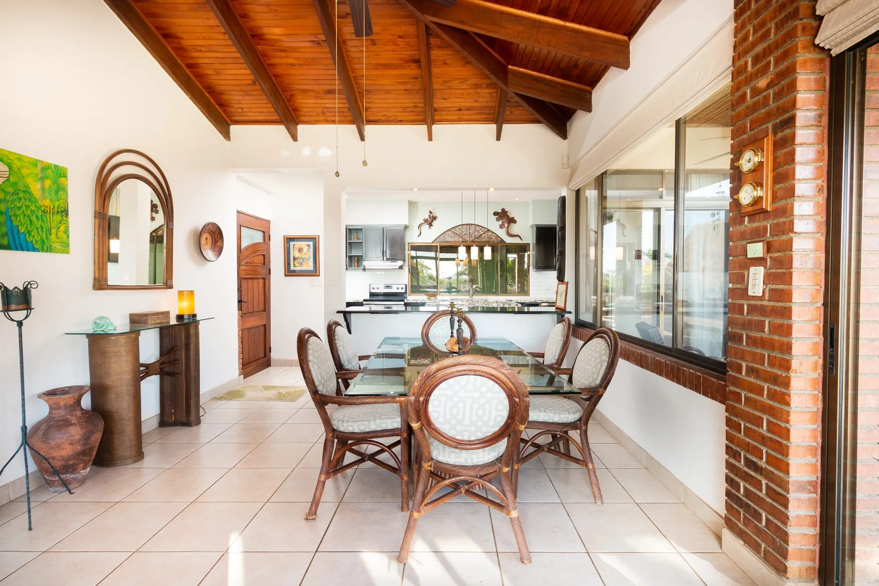 A bright dining area with a glass table beneath a vaulted wooden ceiling.