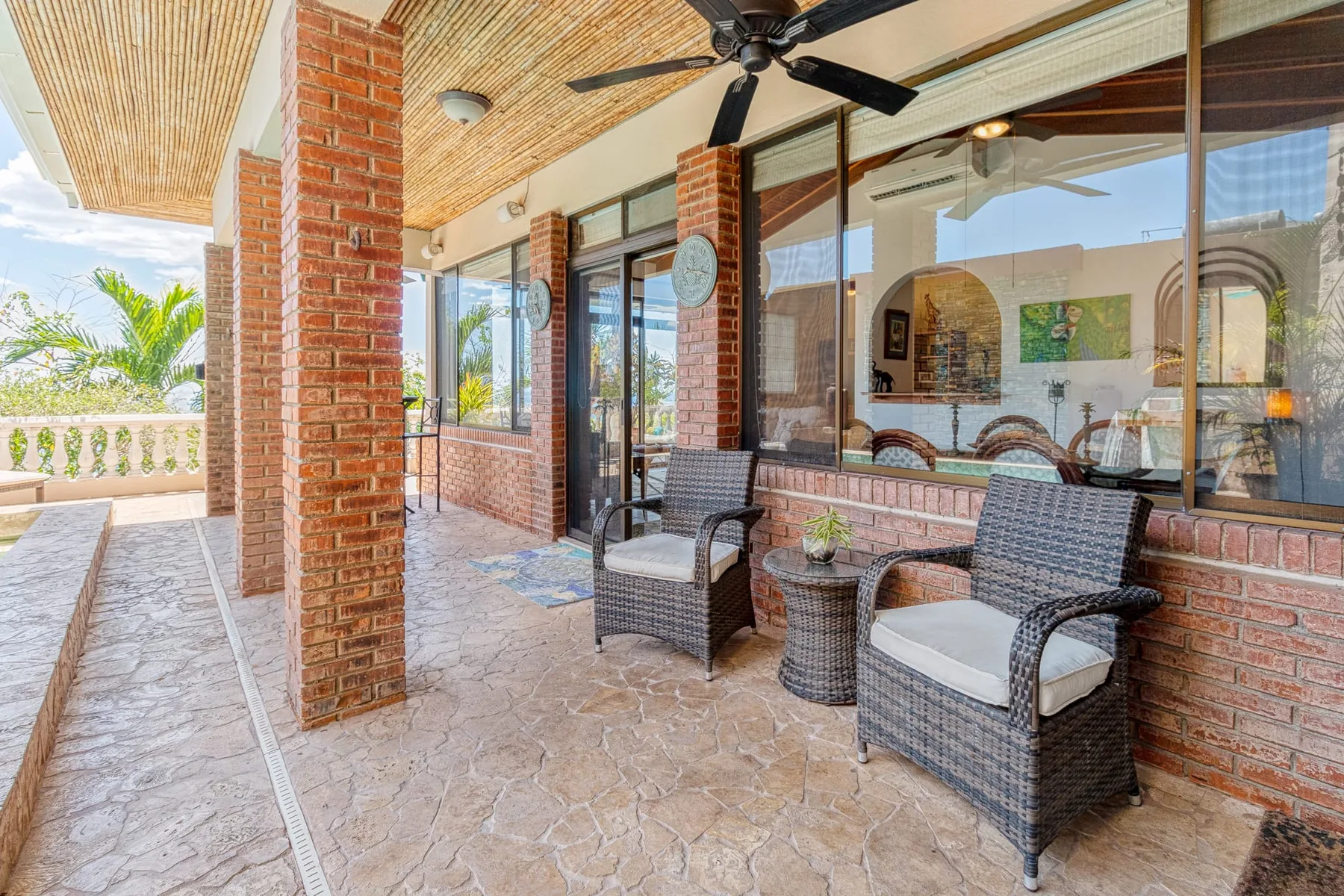 A covered patio with wicker seating faces large glass windows.