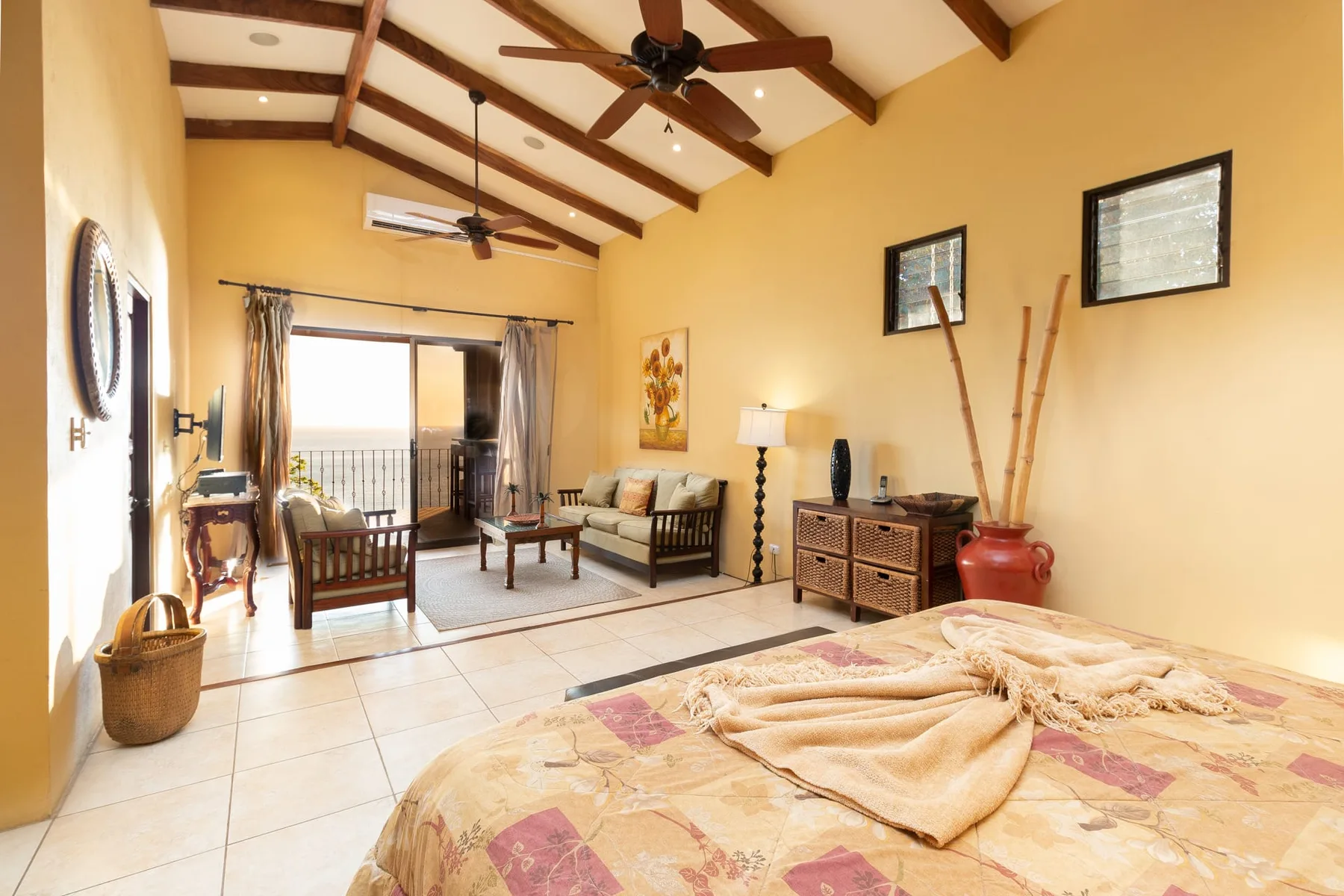A bedroom with a bed in the foreground and a seating area by the balcony doors.