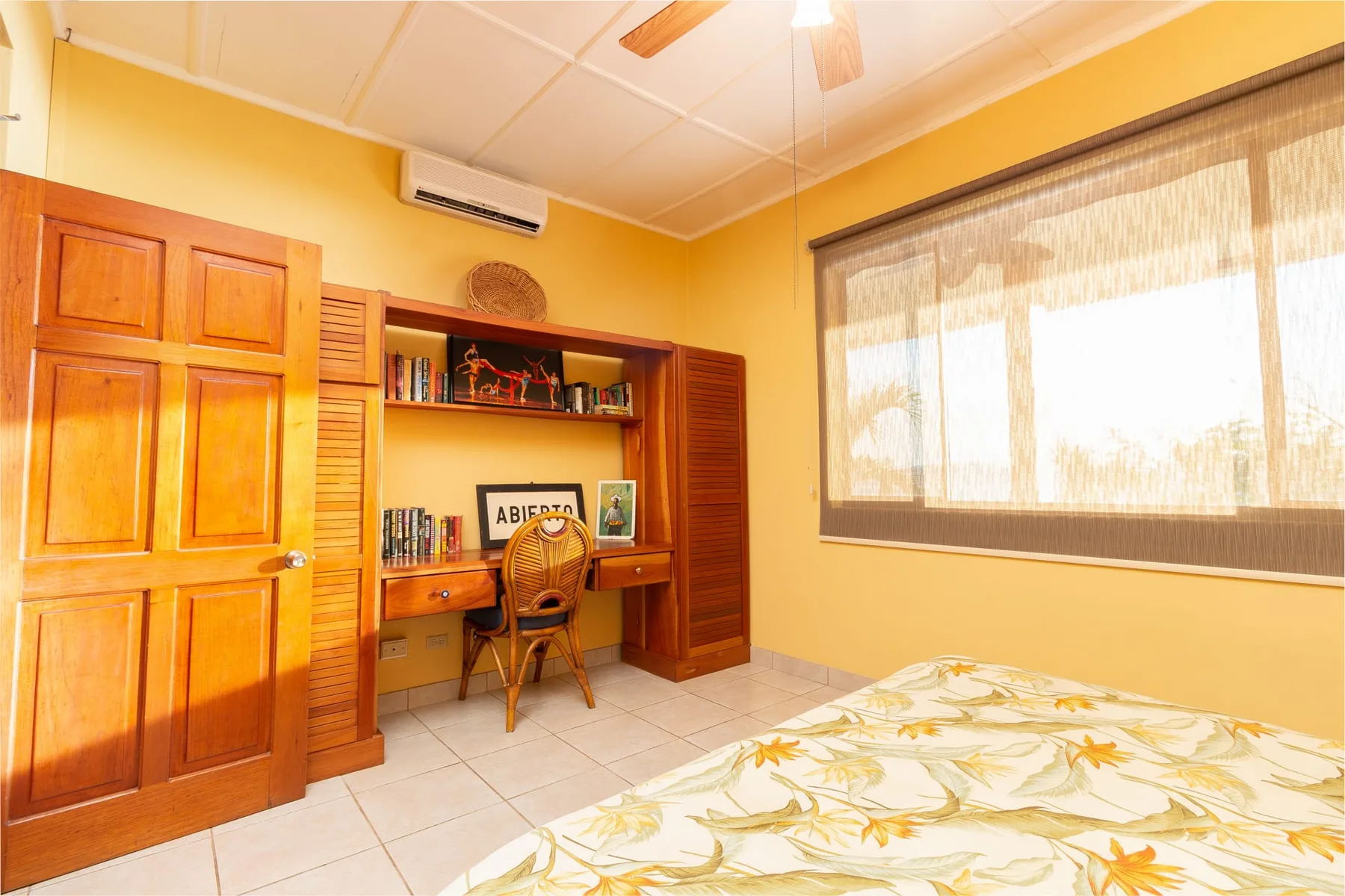 A bedroom with a bed and a built-in wooden desk beneath open shelves.