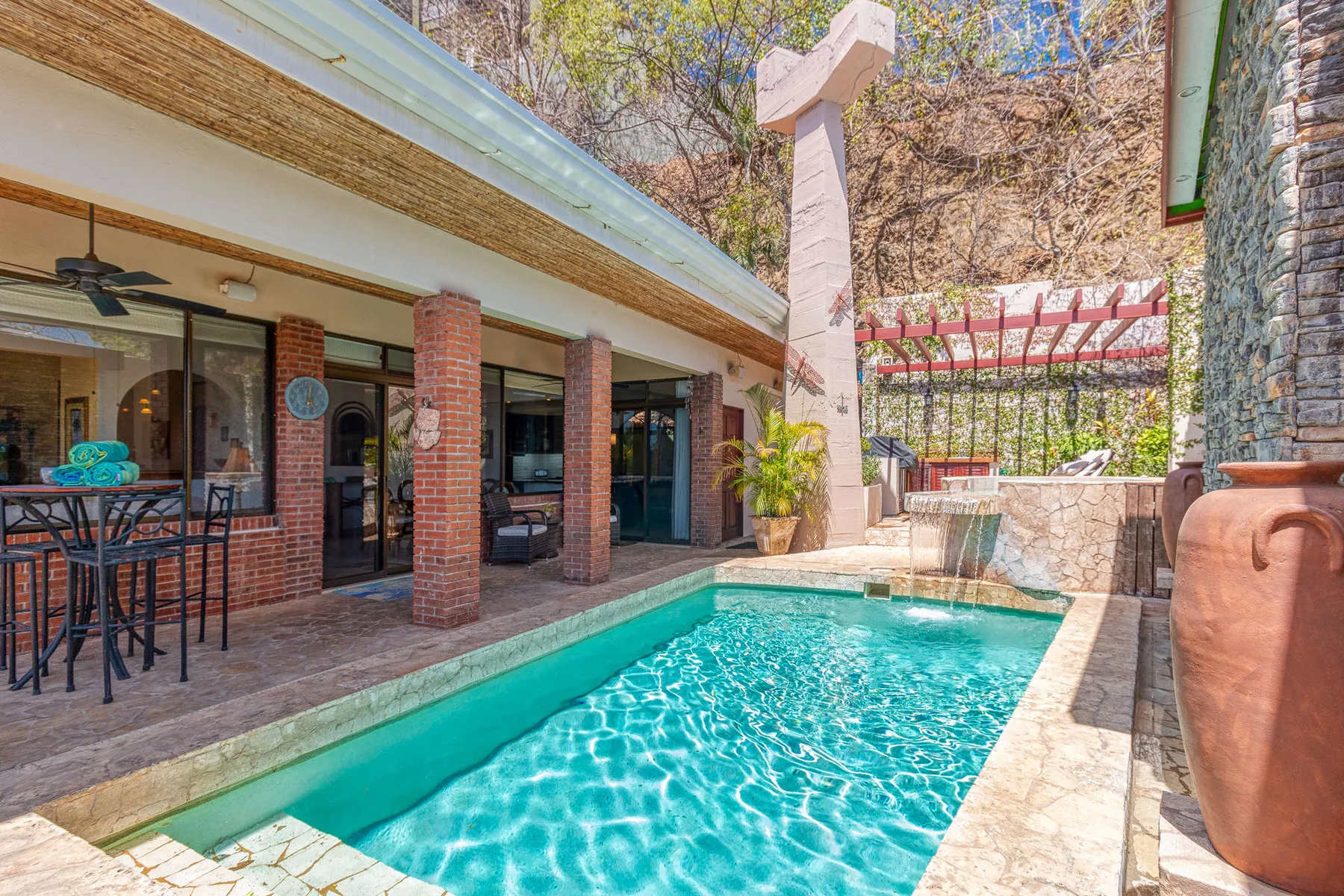 An outdoor swimming pool beside a covered patio with seating.