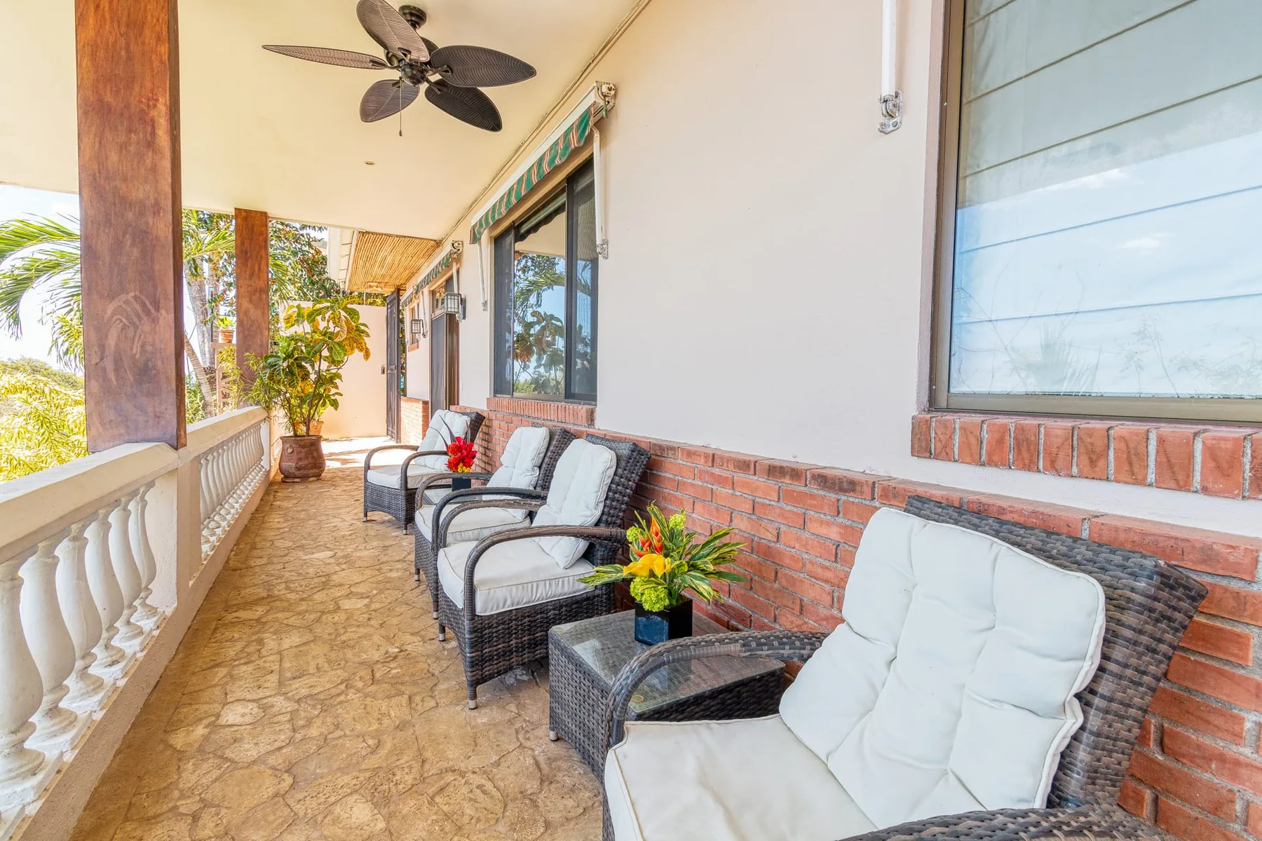A covered outdoor seating area with cushioned chairs and potted plants.