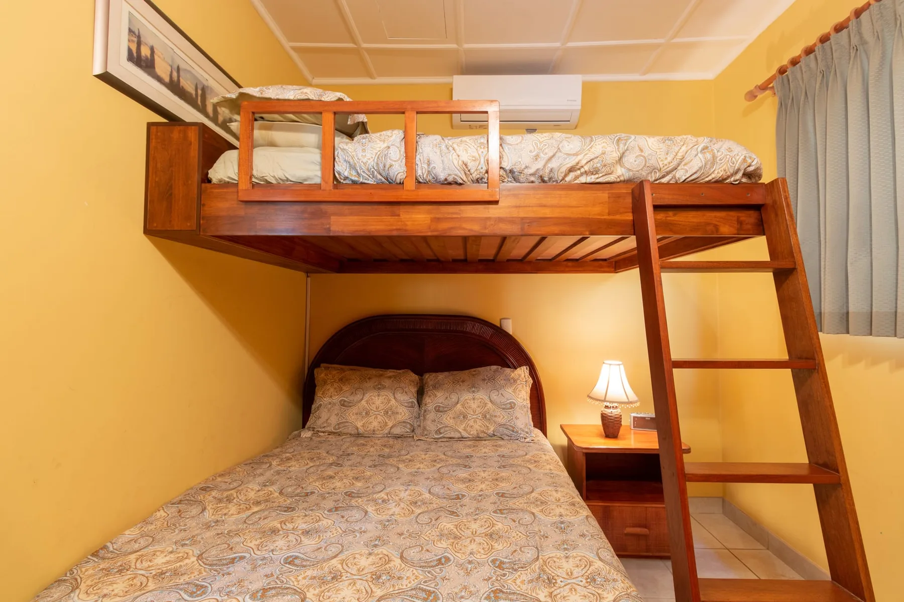 A bedroom with a double-level bed, patterned bedding, and a bedside lamp.