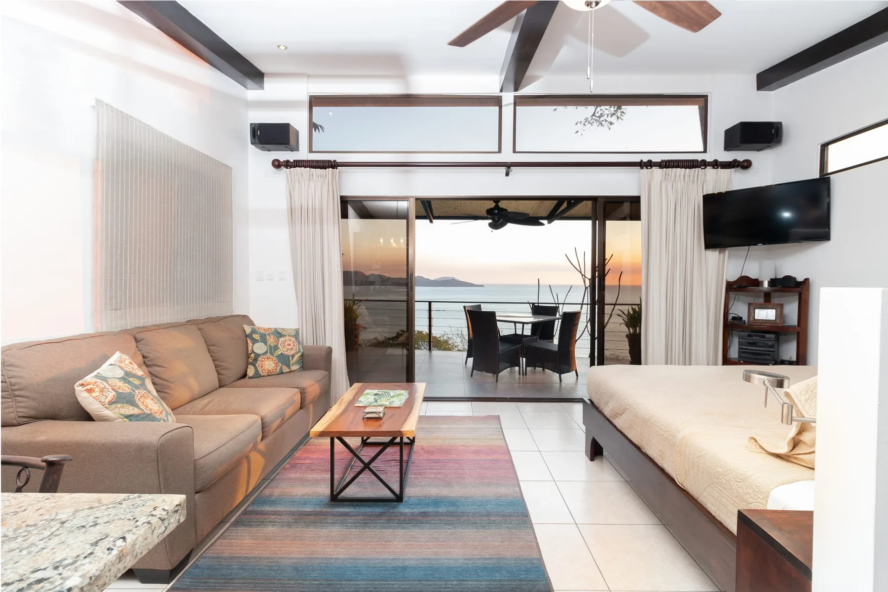 A living room opens onto a balcony, with seating and a dining table overlooking the water.