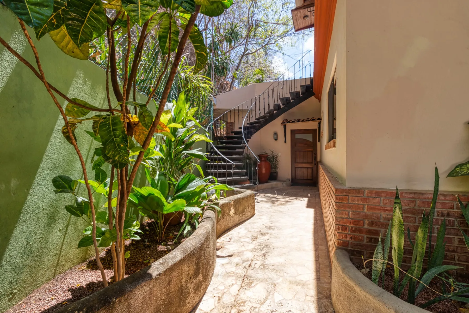A curved outdoor staircase rises beside a garden path and planted beds.