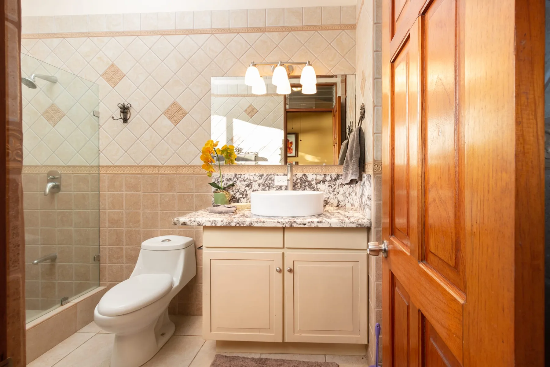A tiled bathroom with a glass shower, toilet, and vanity.