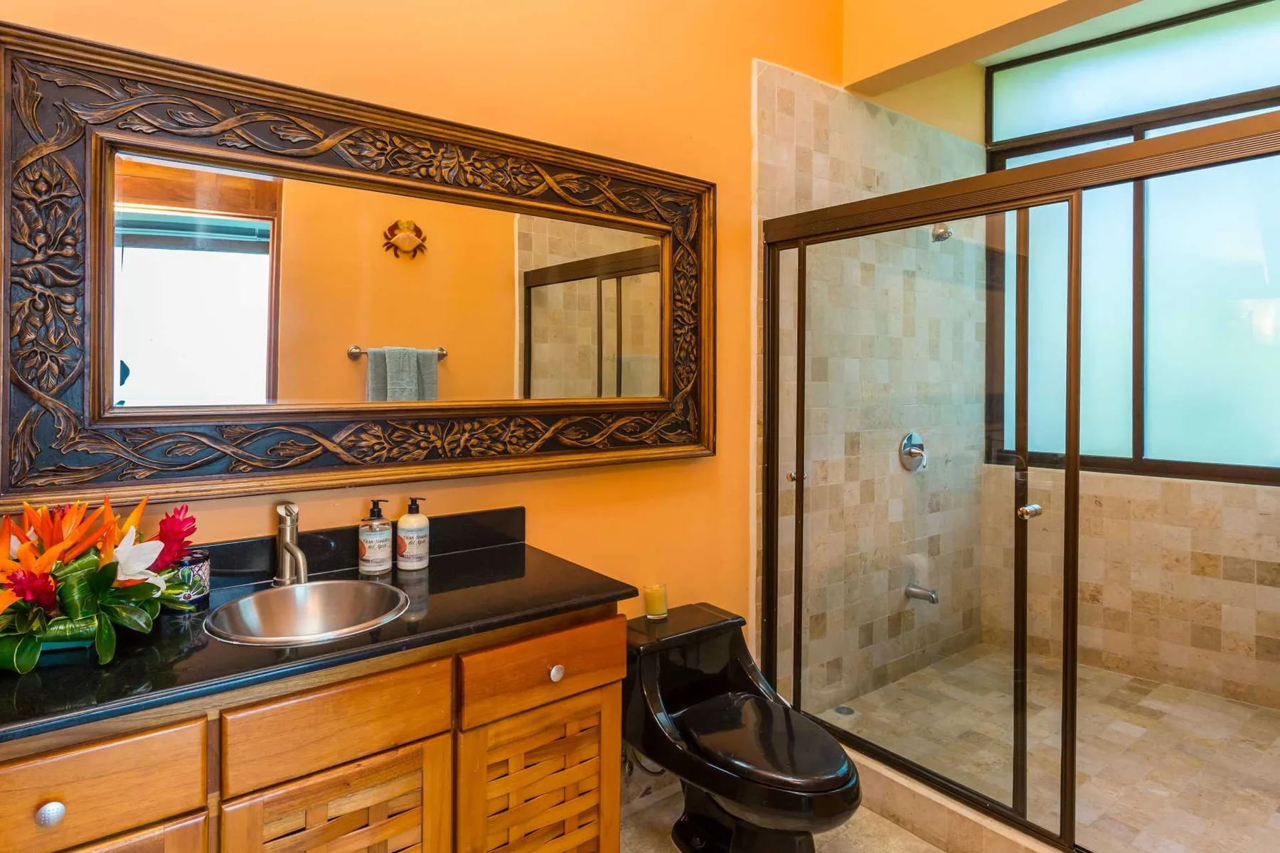 Un baño con tocador de madera, espejo con marco ornamentado y ducha de azulejos con mampara de vidrio.