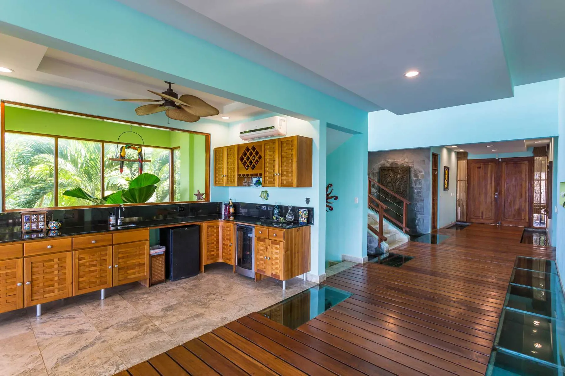 Una cocina turquesa con gabinetes de madera se abre a un pasillo con piso de madera y escaleras.