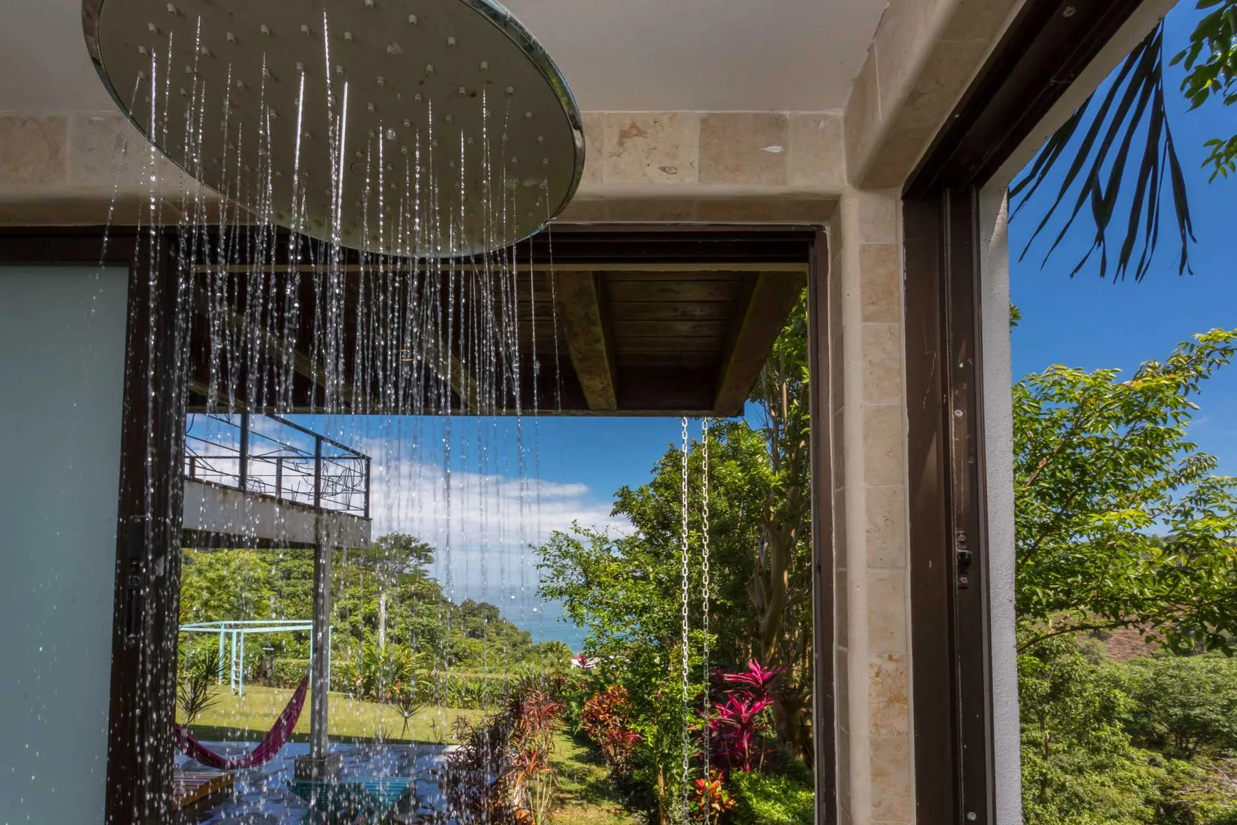 Una amplia ducha de lluvia da a un jardín frondoso a través de puertas de vidrio abiertas.