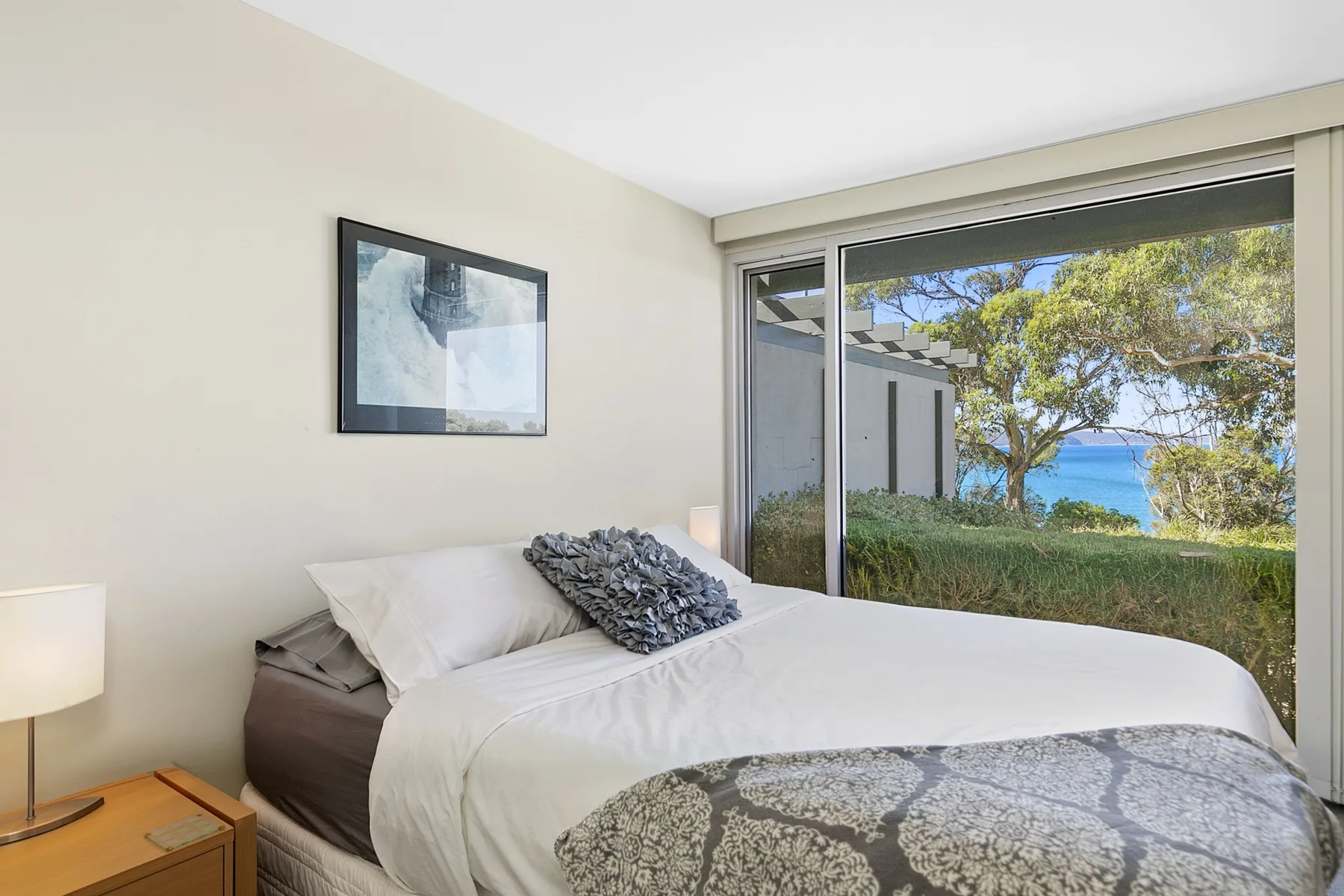 Un dormitorio con una cama bien tendida junto a una gran ventana con vistas a la vegetación.