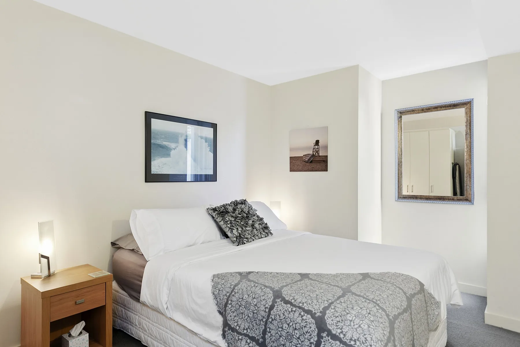 Un dormitorio con una cama bien tendida y cuadros en las paredes.