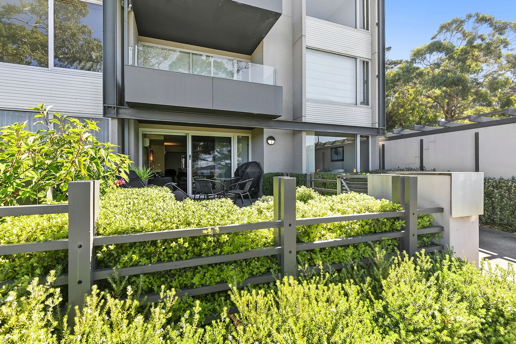 Zona común: Edificio de apartamentos con patio en planta baja y arbustos.